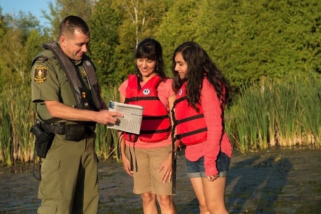 Image d’un agent de protection de la nature montrant le résumé des règlements de la pêche à deux femmes.