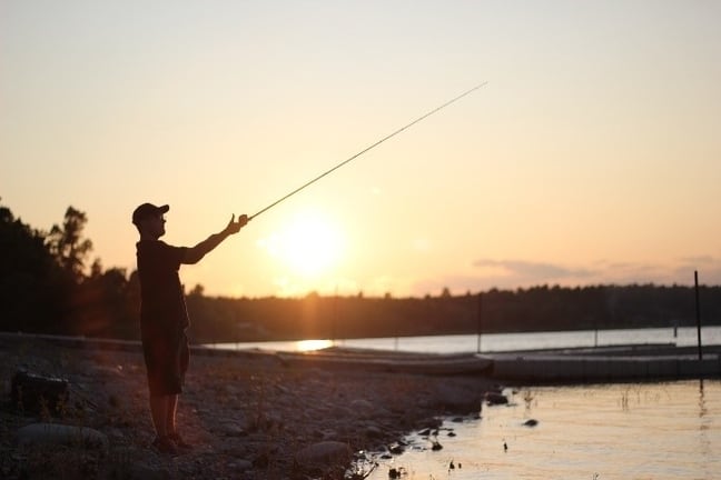 Image d’un homme lançant sa ligne du rivage alors que le soleil se couche.