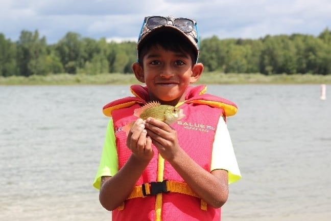 Image d’un garçon portant un gilet de sauvetage et tenant un petit poisson, tout sourire.