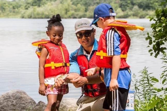 Image d’un guide Apprenez à pêcher montrant à deux enfants comment tenir un petit poisson.