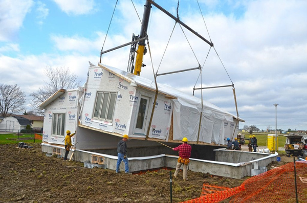 A module being lowered by crane onto a foundation while workers help to secure the module in place