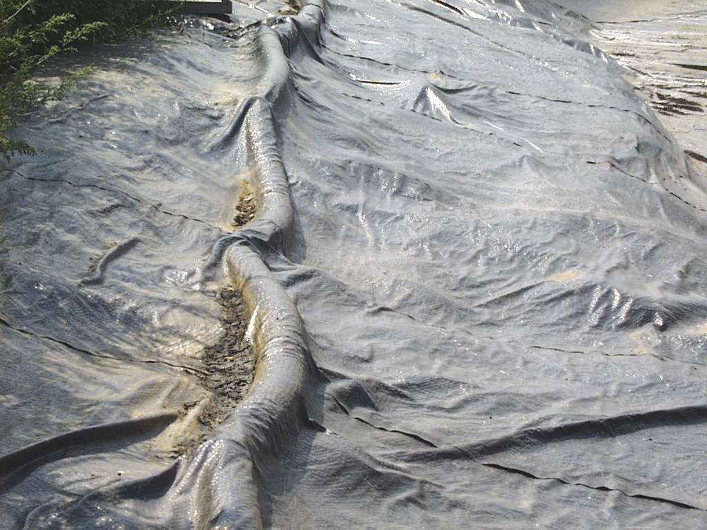 Earthen manure storage cover showing the pipe that is drawing the air out from under the cover, with the cover being pulled down tightly to the surface