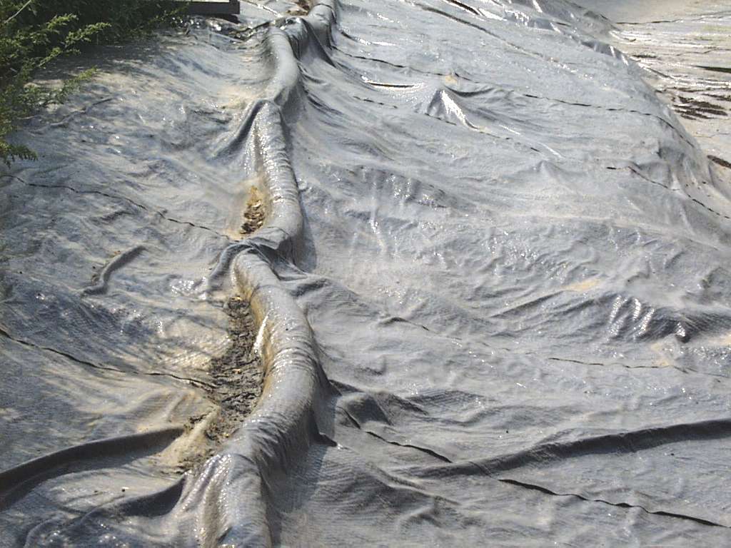 Couverture d’une structure de stockage de fumier en terre montrant le tuyau qui aspire l’air se trouvant sous la couverture, avec la couverture tirée vers le bas tout contre la surface