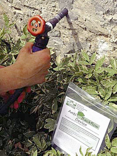 Anti-backflow device installed on an outdoor faucet and a hand holding the hose