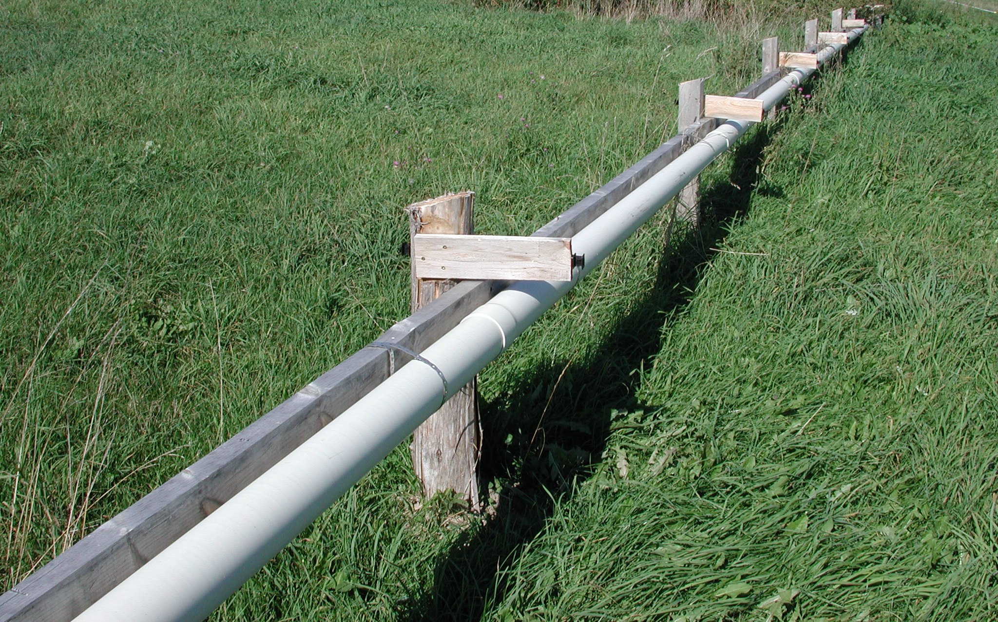 Close up picture of a pipe running out into a field. The pipe contains evenly spaced 1.9 centimetre (3/4 inch) holes which allow for distribution of the runoff in to the field.