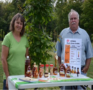Farm owners standing behind a table displaying the maple syrup products they produce. 