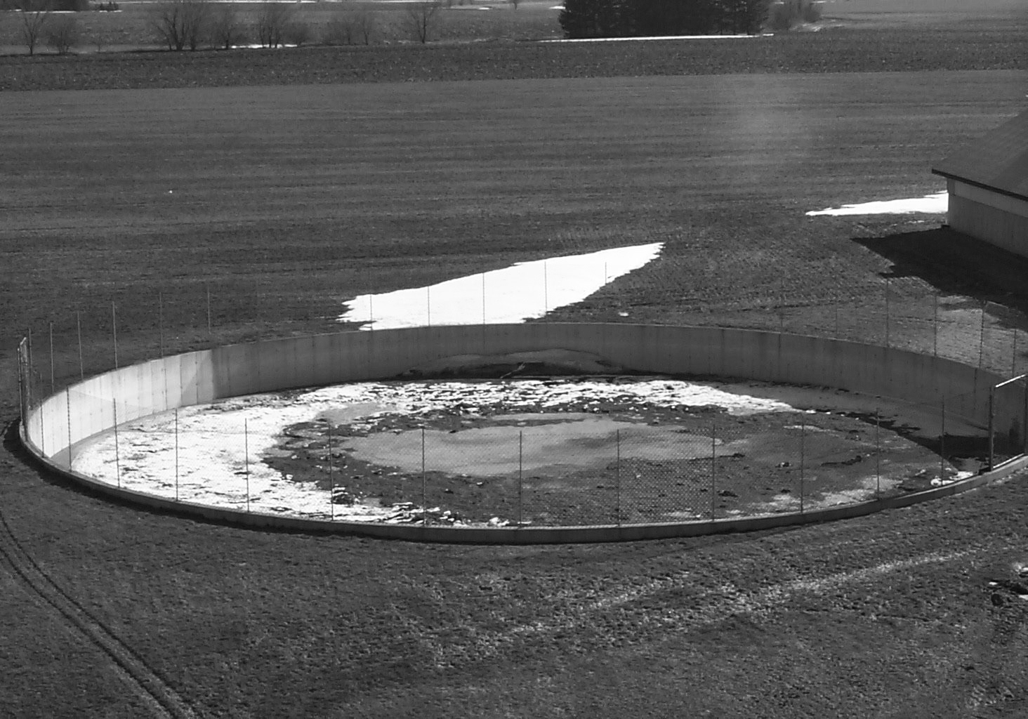 Photo d’un réservoir circulaire à ciel ouvert, pour l’entreposage de fumier liquide, dans un champ. Le réservoir est entouré d’une clôture en acier.
