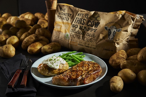 An image of loose potatoes with a bag of The Honest Potato Company potato bag is in the middle of the photo. There is a plate with potato, meat and green beans in the foreground of the photo.