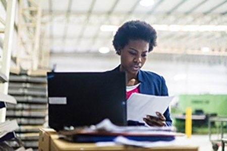 Image of a woman reading a paper while working on a laptop