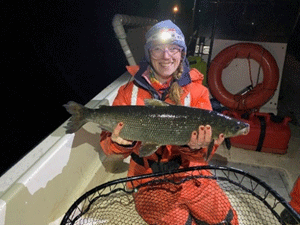 A person seated in a boat, holding a large fish