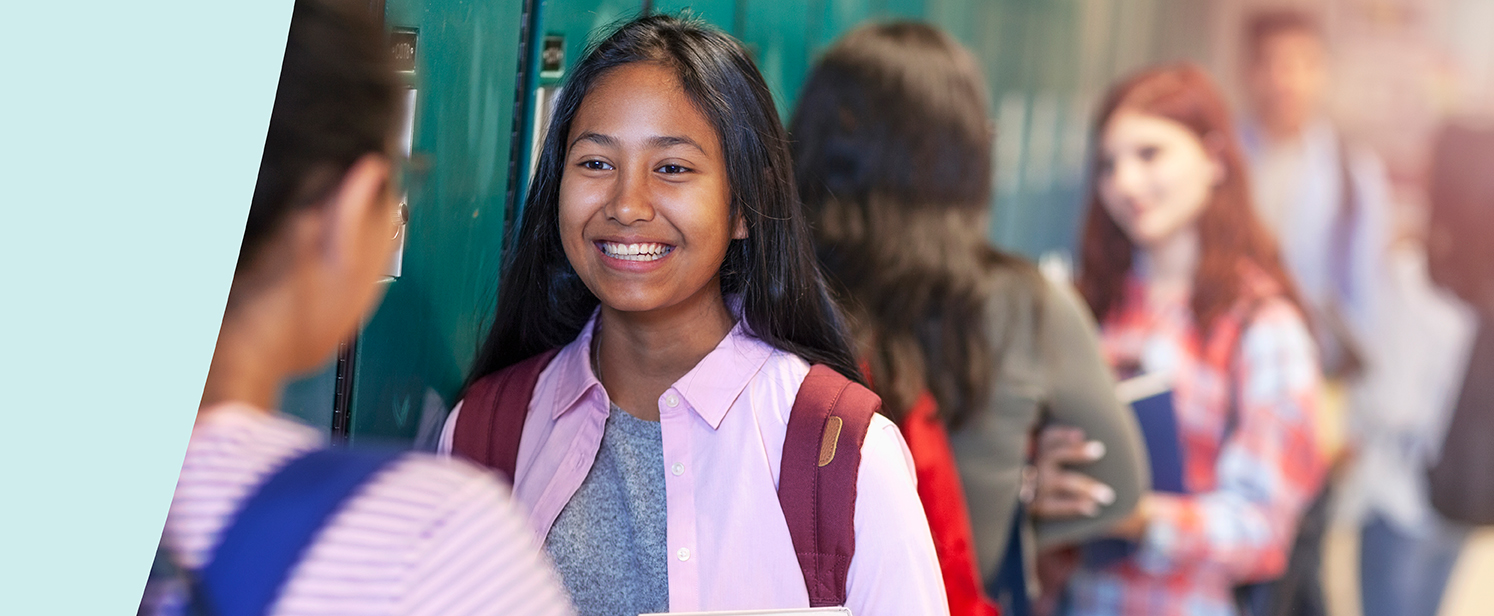 Students chatting and smiling in a school hallway by lockers.
