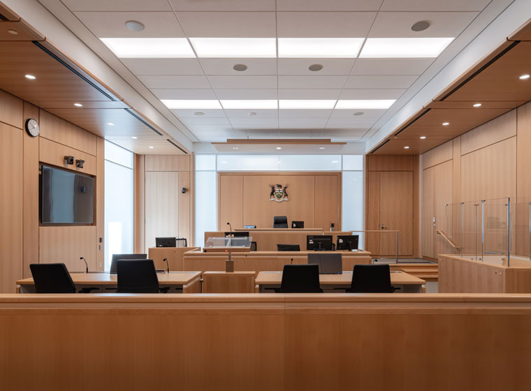 Inside of a courtroom with wooden benches and black chairs.