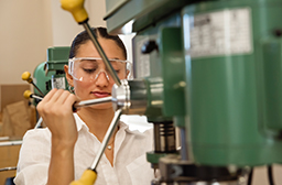 A young student wearing protective eye wear and operating a drill press.