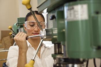 A young student wearing protective eye wear and operating a drill press.