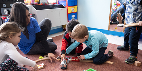 A woman child care worker supervising young children who are playing with a train set in a child care centre.