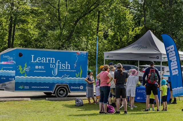A group of individuals across all ages in front of the learn to fish mobile unit