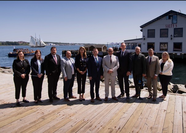 Photograph of a group of federal, provincial, and territorial ministers standing in a line on a wooden dock in front of a white building and waterfront, at the MCCF August meeting.