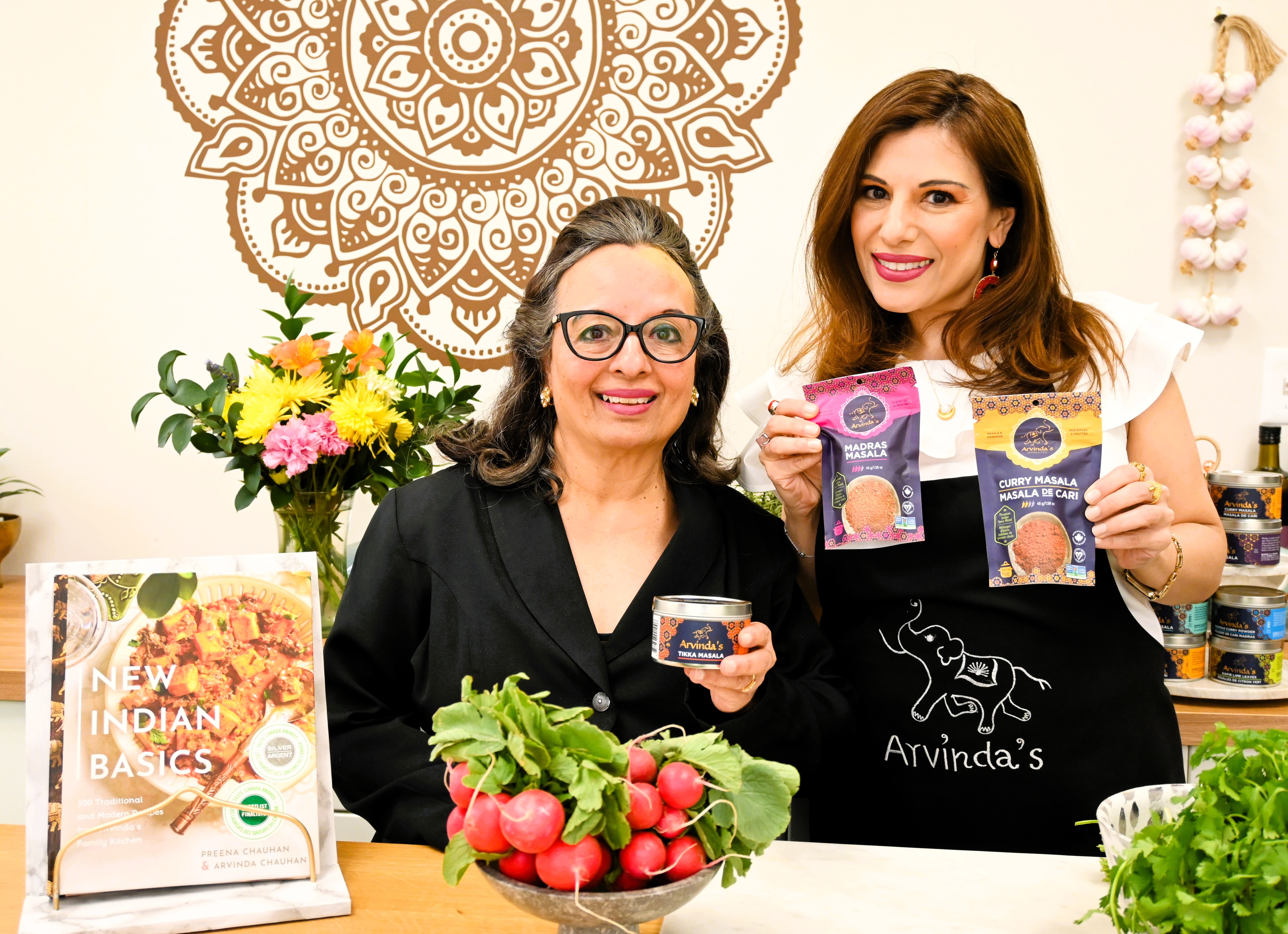 An image of two women holding Indian spices. There is a bowl of radishes and greens in front of them.