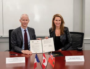 Photograph of Ontario’s Minister of Francophone Affairs, Caroline Mulroney, and Franck Riester, France’s Minister Delegate for Foreign Trade, Attractiveness, Francophonie and French Nationals Abroad, seated side by side behind a wooden table holding a signed joint declaration; three small flags (France, Canada, Ontario) are displayed in the foreground