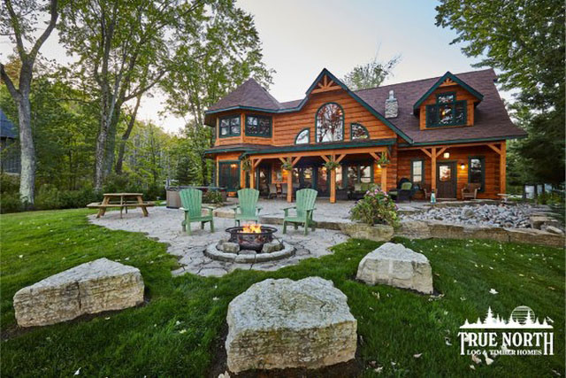 Une large pelouse devant une maison en bois rond avec un foyer.