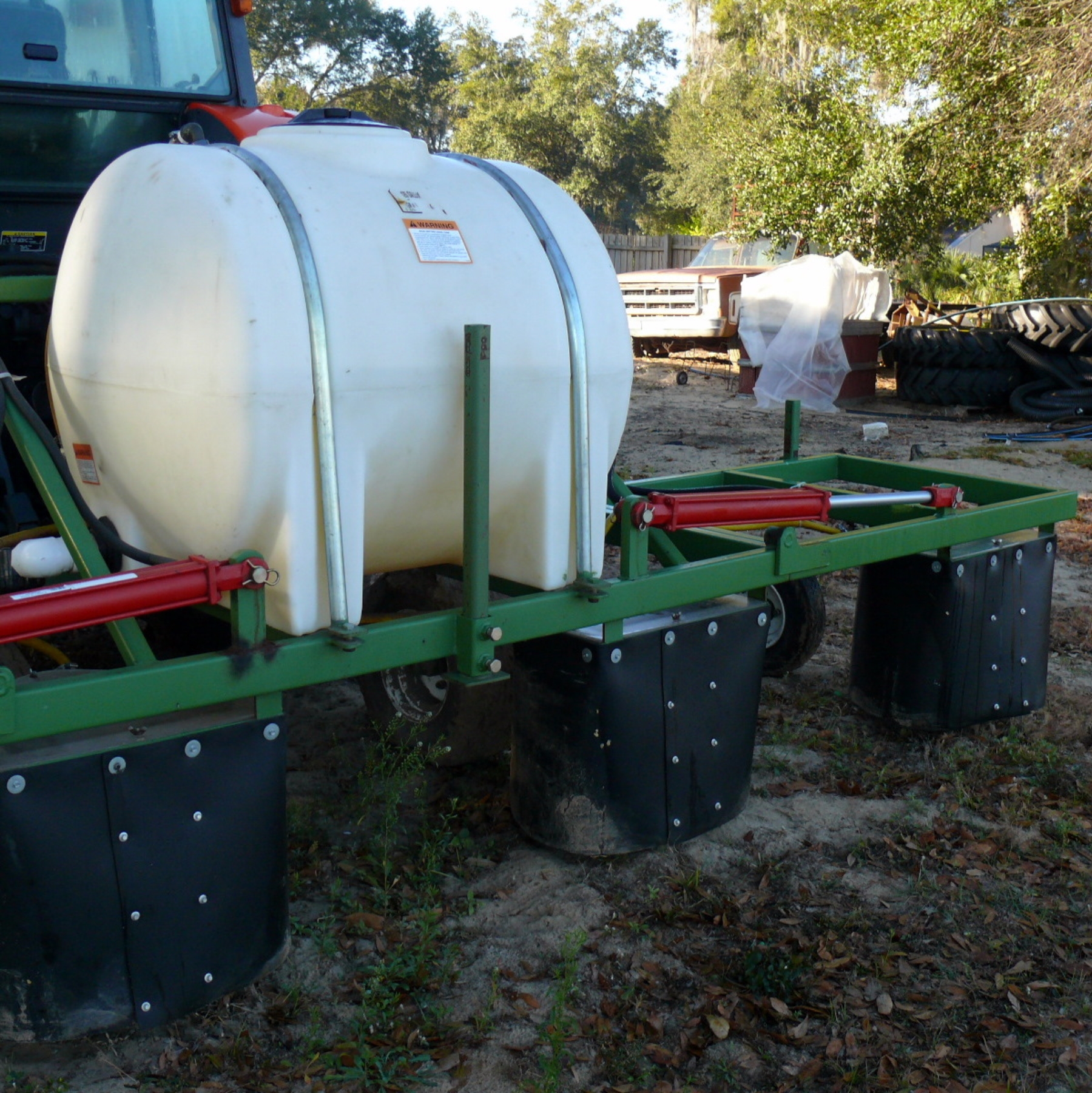 Shrouds on a horizontal boom. The shrouds are black covers that surround the nozzles. They hang below the metal frame of the sprayer and under the sprayer tank.