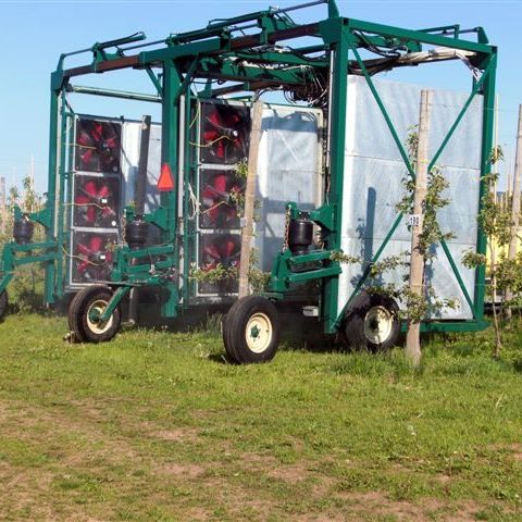 A recycling sprayer. This features a square implement that fits over the rows and stakes of an orchard. The sprayer is green and on wheels and features fans on the internal walls of the implement.