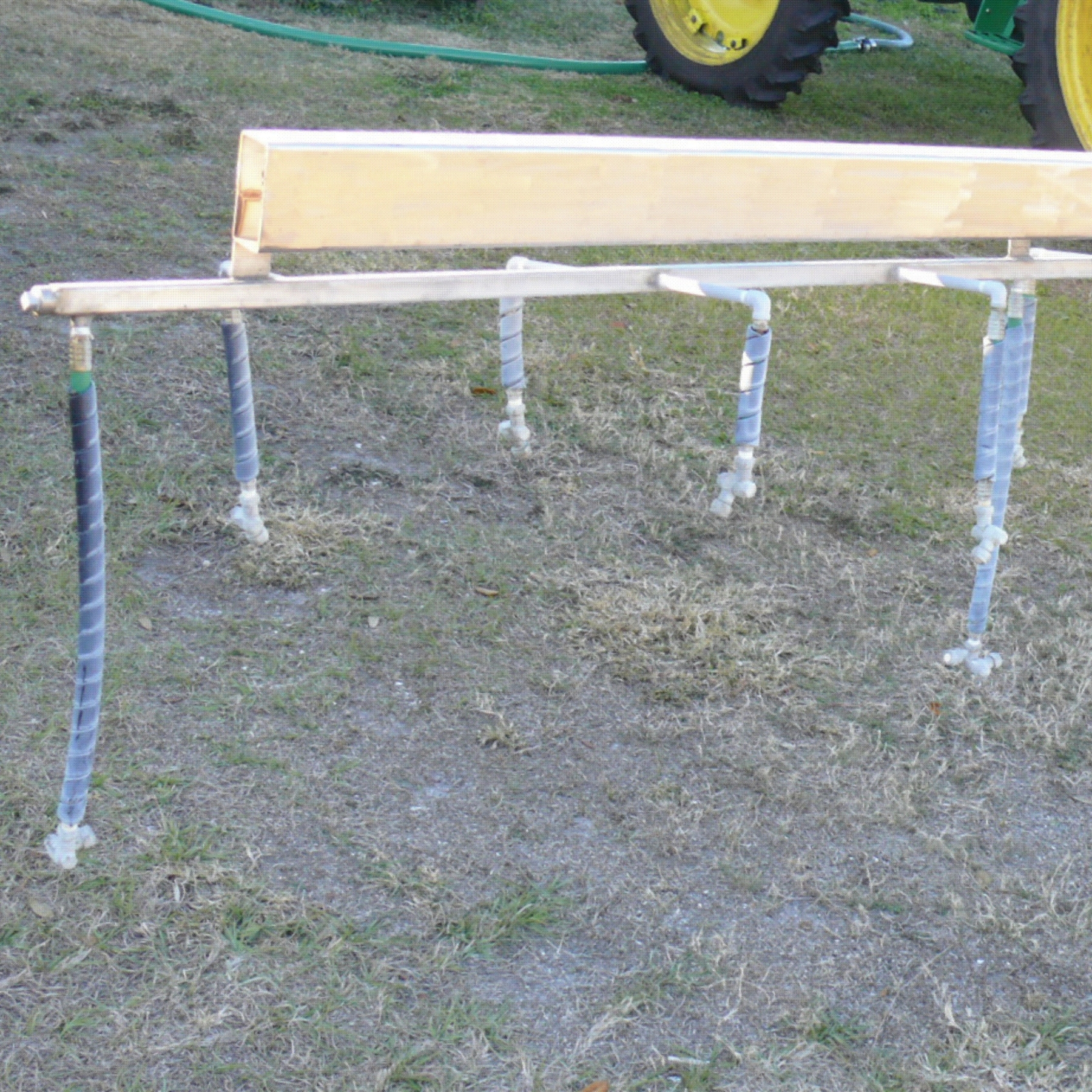 Drop arms on a horizontal boom. The drop arms are blue tubes hanging down from a boom on a wooden arm. The blue tubes have nozzles at the end.
