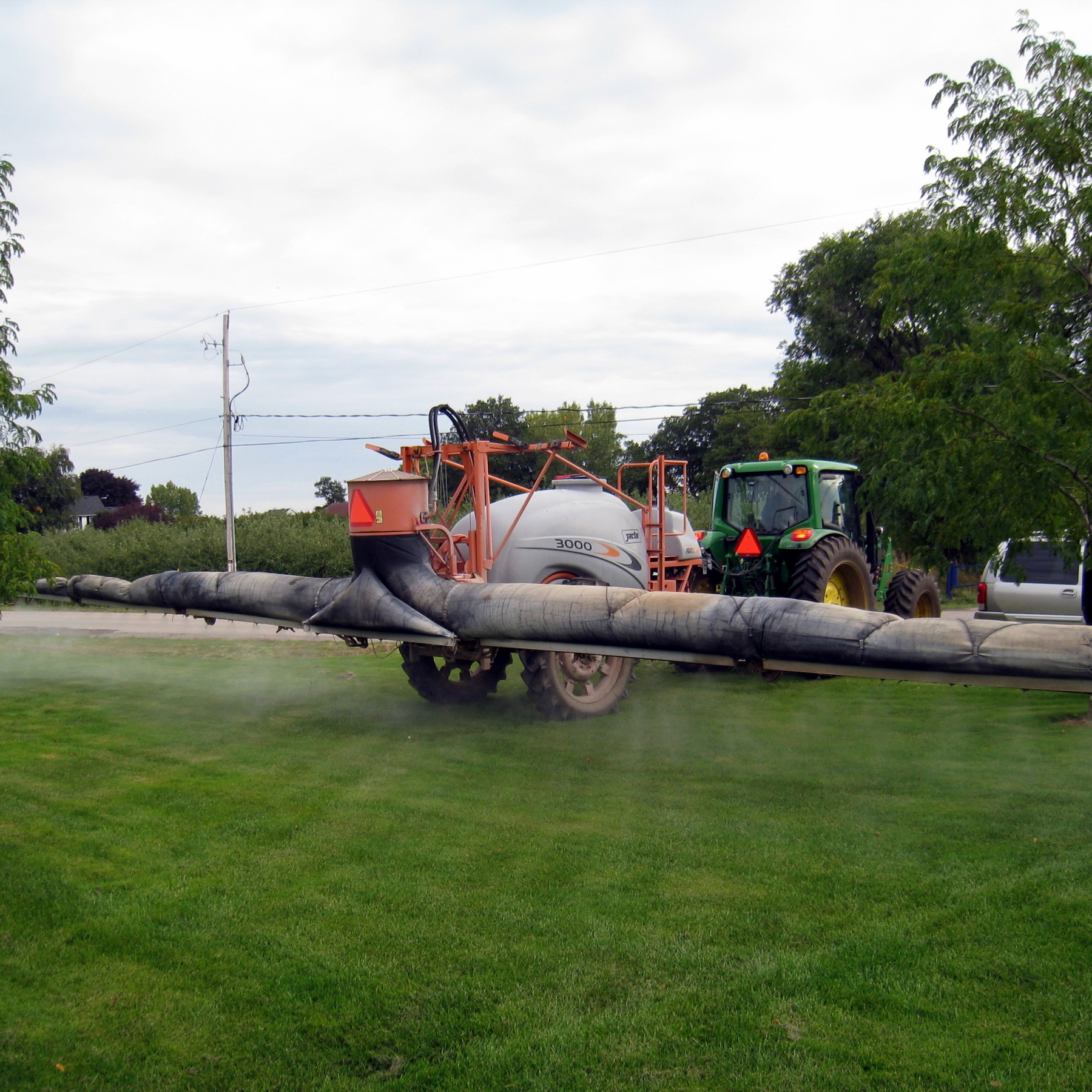 Air-assist sleeve on a horizontal boom. The air-assist sleeve is an inflatable cover that covers the entire boom. This is attached to a sprayer tank that is attached to the back of a tractor. 