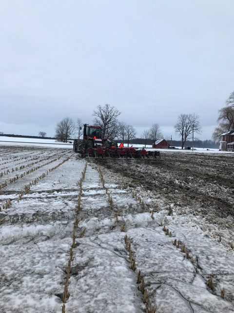 un tracteur qui tire une herse à disque sur du sol gelé un peu enneigé afin d’y incorporer du fumier