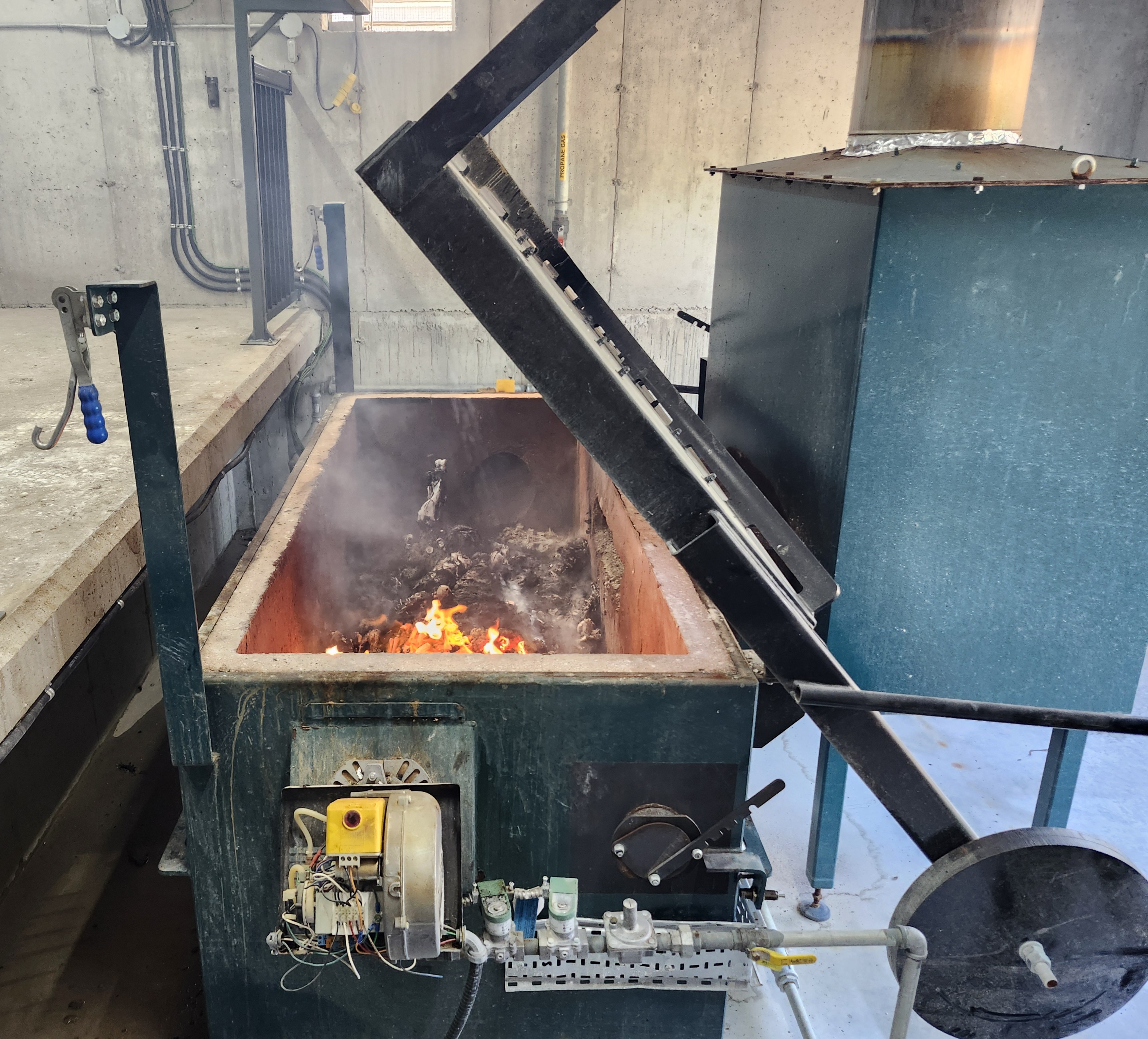 Incinerator with secondary chamber. Lid of primary chamber is open to show material being incinerated