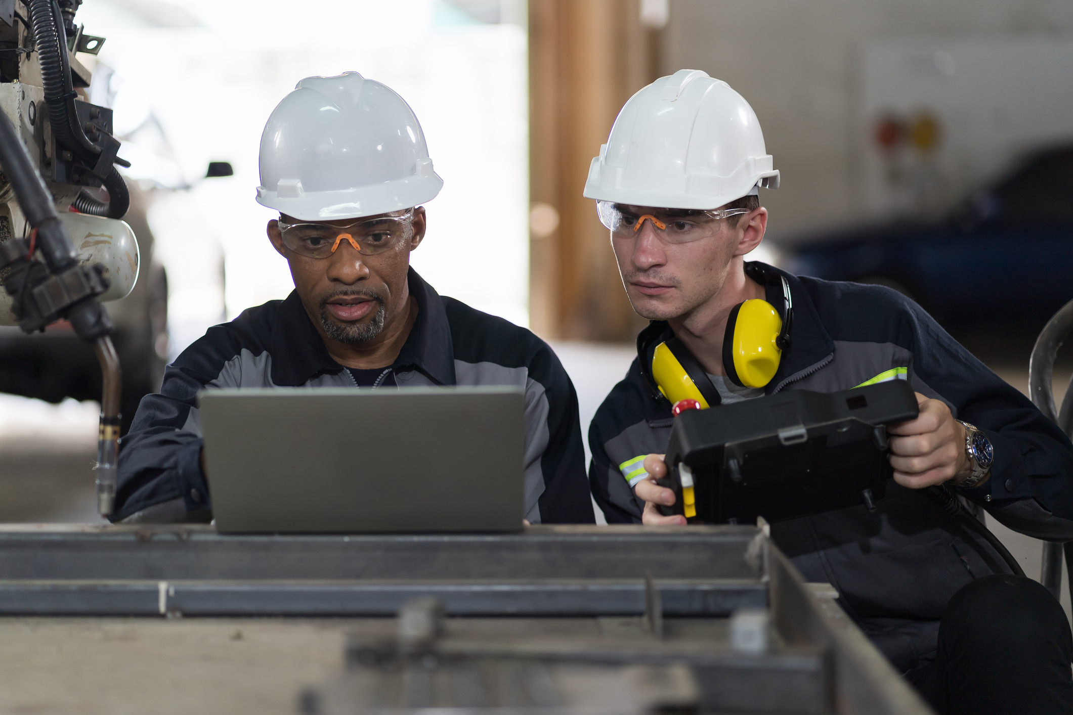Deux techniciens portant un casque protecteur et des lunettes de protection qui lisent de l’information sur des ordinateurs dans un milieu industriel.